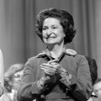 Former first lady, Lady Bird Johnson, wearing a Viva La Mujer button, smiling and clapping.